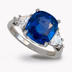 Classic Three Stone Sapphire & Diamond Ring Designed and Handmade by Kaufmann de Suisse in Platinum featuring one Cushion Cut 4.87cts Blue Sapphire flanked by two H/VS Quality Triangle Diamonds weighing a total of 1.00cts